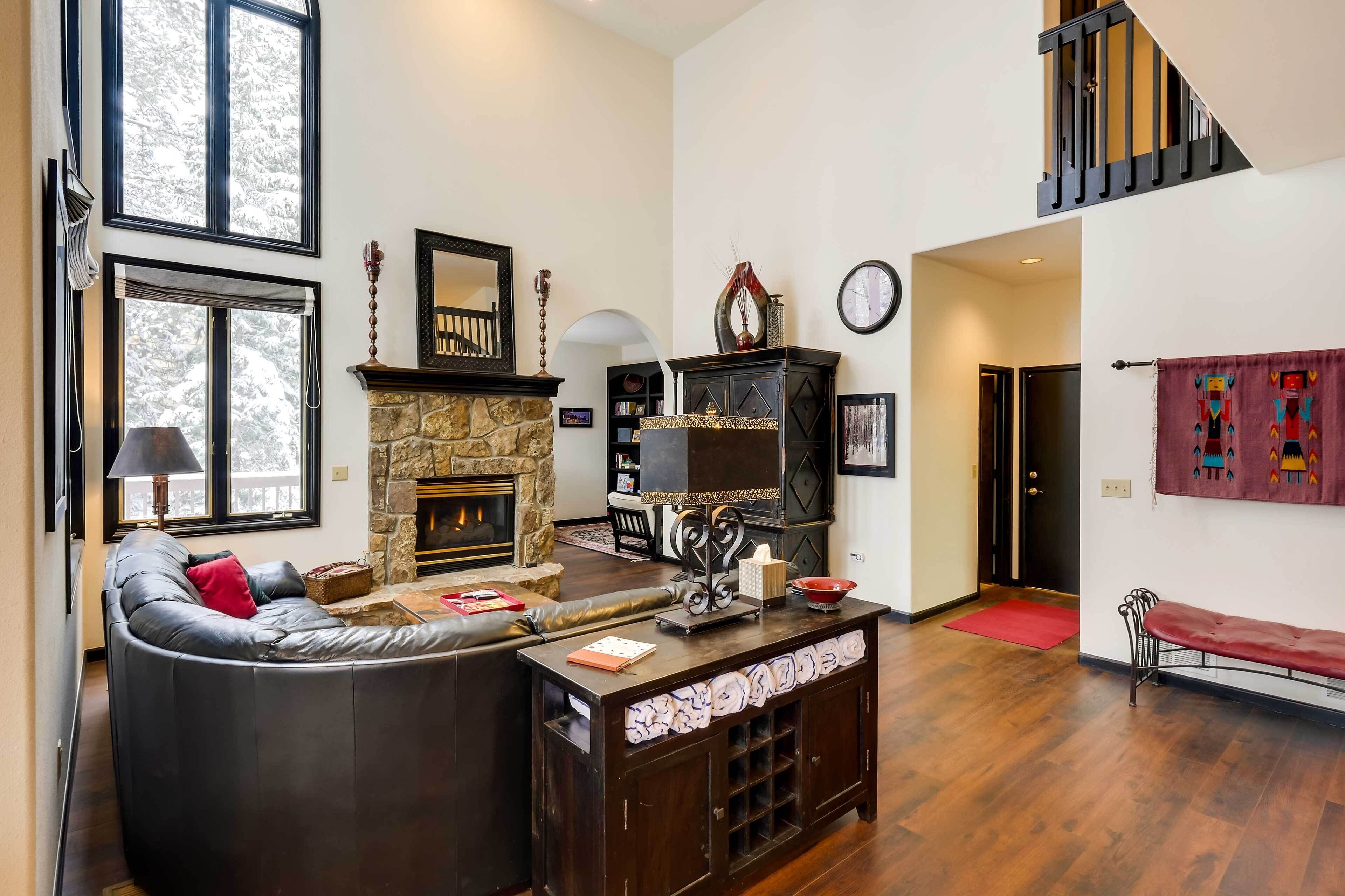 A spacious living room with a stone fireplace, a black leather sofa, and a wooden coffee table.