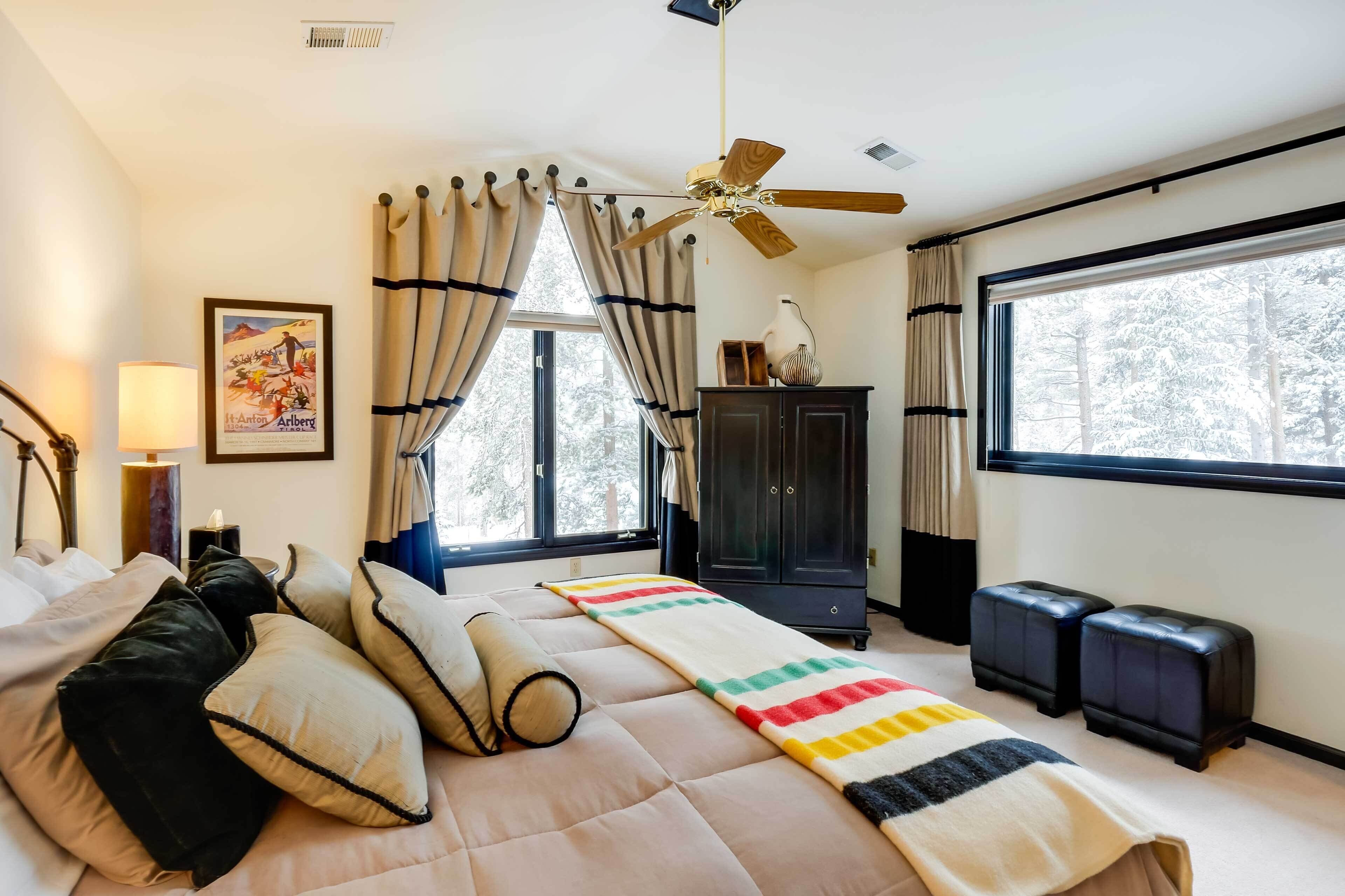 Une chambre à coucher comprenant un lit, un ventilateur de plafond, une fenêtre avec des rideaux, une armoire et une table de chevet avec une lampe.