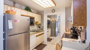 A modern kitchen with stainless steel appliances, a wooden ceiling light, and a view into the adjacent dining area.