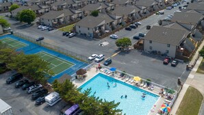 A residential area with a swimming pool, tennis court, and multiple parked cars.
