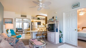 A cozy living room with a sofa, a glass-top coffee table, and a dining area with chairs and a TV.
