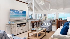 A spacious living room with a large TV, wooden furniture, and a view of the ocean. - Villa Calypso: Ocean Access, Pool, Kayaks, & More! (Providenciales)