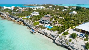 A coastal property with a swimming pool, a dock, and a view of the turquoise sea and clear skies. - Villa Calypso: Ocean Access, Pool, Kayaks, & More! (Providenciales)