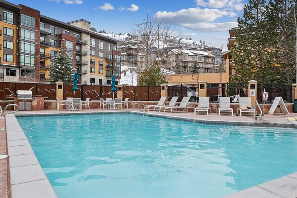 A swimming pool with lounge chairs and a barbecue area, surrounded by multi-story buildings with balconies.