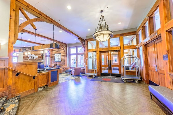 A spacious lobby with wooden architecture, a reception desk, seating area, and a chandelier.