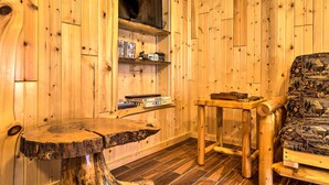 Ein Holzinnenraum mit einem runden Tisch, einem Stuhl und einem Regal mit Büchern und einem Radio.