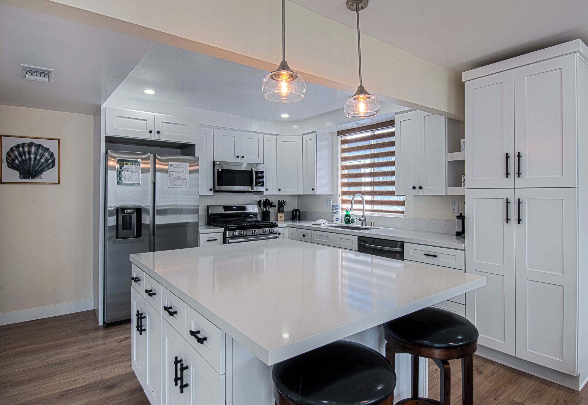 Una cocina moderna con gabinetes blancos, electrodomésticos de acero inoxidable, una isla grande e iluminación colgante.