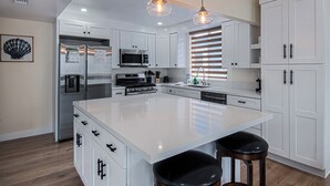 A modern kitchen with white cabinetry, stainless steel appliances, a large island, and pendant lighting.