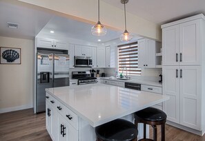 Uma cozinha moderna com armários brancos, eletrodomésticos de aço inoxidável, uma ilha grande e iluminação pendente.