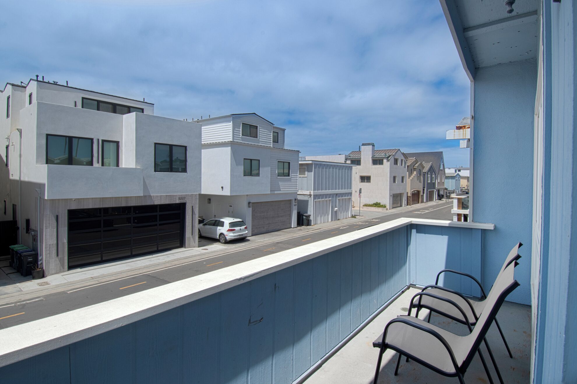 A modern building with a garage, a white car parked outside, and a balcony with chairs.
