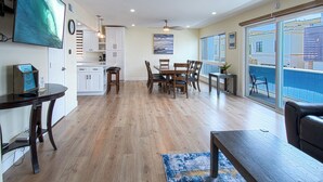 A spacious living area with a dining table, wooden flooring, and a view of a swimming pool through large sliding doors.
