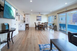 Uma sala de estar ampla com mesa de jantar, piso de madeira e vista para uma piscina através de grandes portas deslizantes.