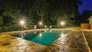 Ein Pool mit Steinplatten, umgeben von einem Zaun und Bäumen, mit Beleuchtung.