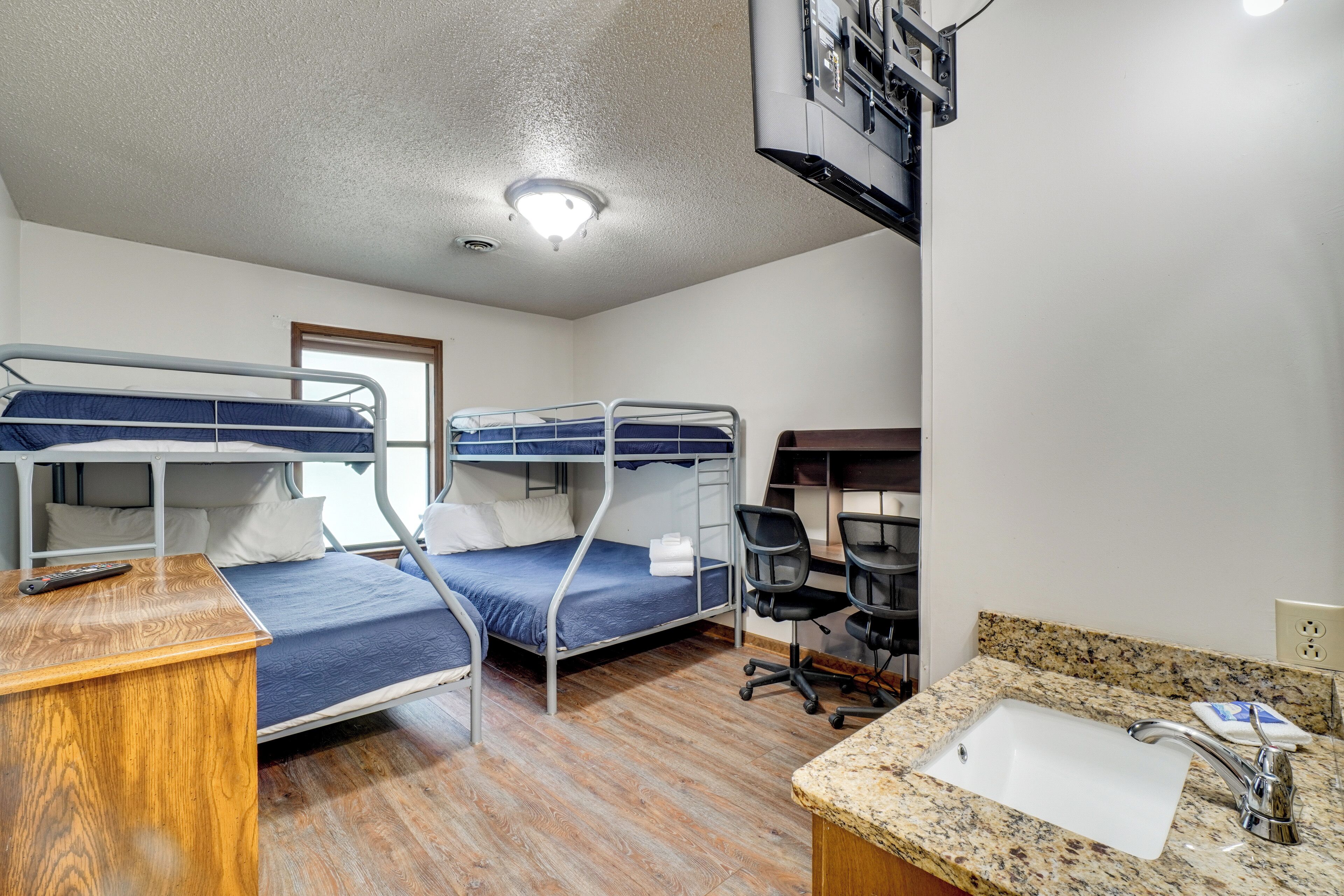 A dormitory room with bunk beds, a desk, a chair, a sink, and a mirror.