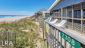 Un bâtiment situé en bord de mer, doté d’une terrasse en bois, portant le numéro 2308 et offrant une vue sur la plage.