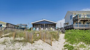 Une propriété située en bord de mer, avec une grande maison dotée d’un porche et d’un espace couvert, le tout entouré de sable et de végétation.