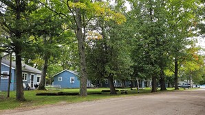 A blue house with a fenced yard, a dirt path, and trees. - Family resort cottage 3 on Big Glen Lake, Rent 1 or 5, dock, kayaks, rowboat (Maple City)