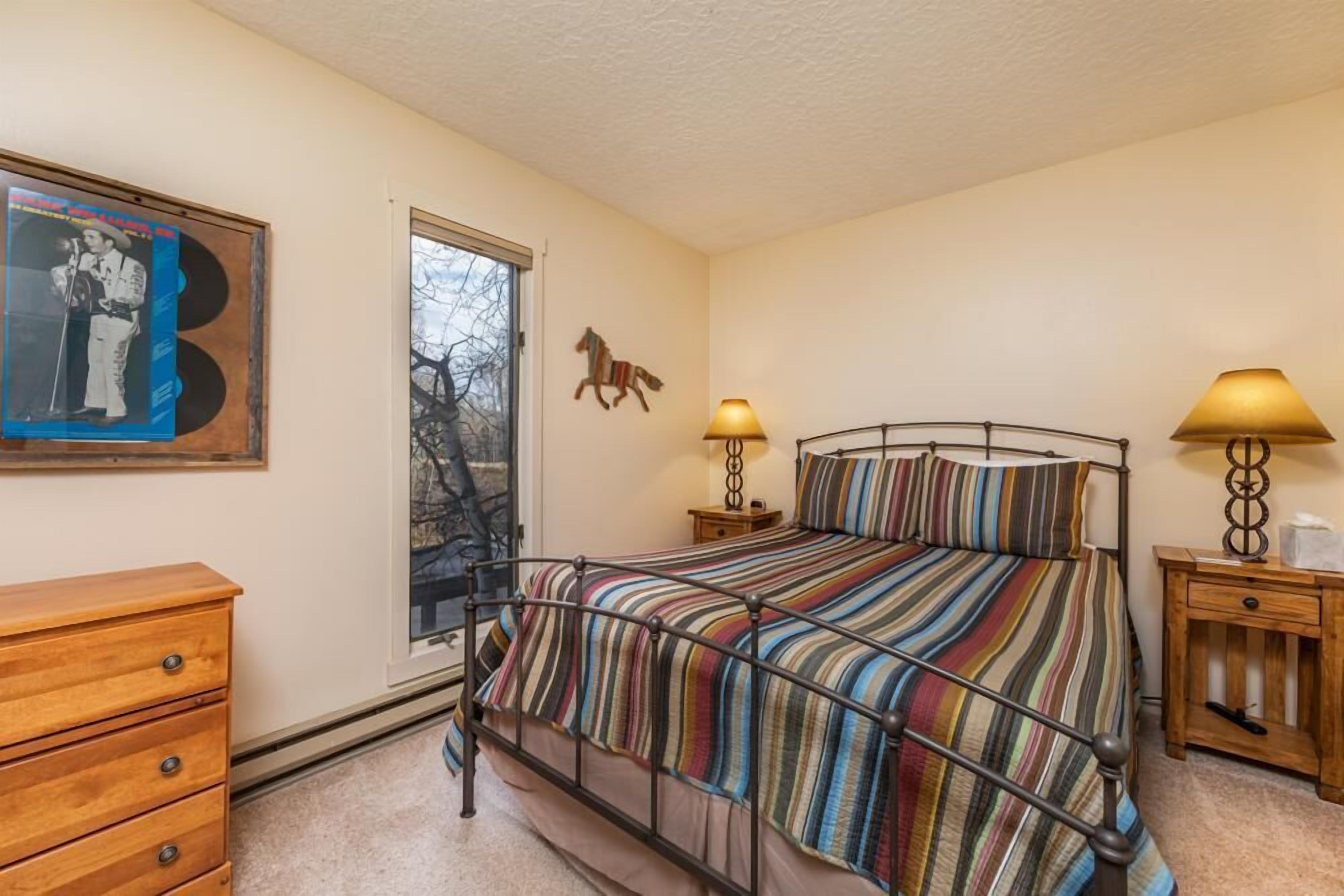 A bedroom with a metal bed frame, a striped bedspread, a wooden dresser, a wall-mounted horse decoration, and a poster on the wall.