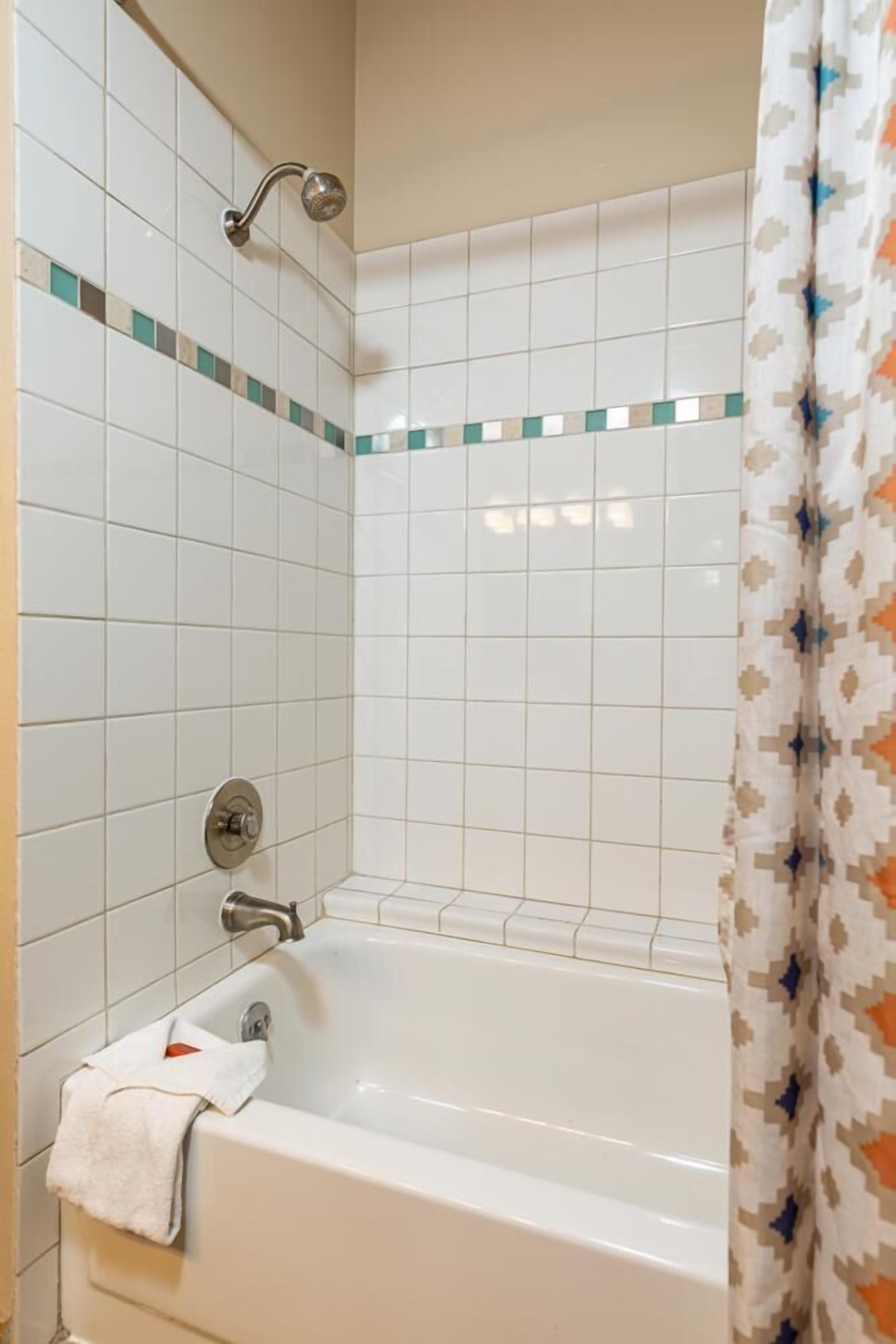A bathroom with a bathtub, a showerhead, and a towel on the floor.