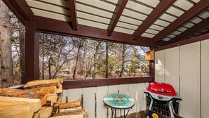 Un espacio al aire libre techado con una parrilla, una mesa con cubierta decorativa y una pila de leña.