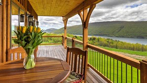 Un terrazzo in legno con tavolo e sedie, un vaso di tulipani gialli e vista su un lago e montagne.