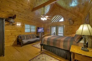 Quarto de cabana de toras com uma cama, um sofá, uma televisão e um ventilador de teto.