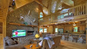 L’intérieur d’un chalet rustique, avec une cheminée en pierre, un téléviseur, un canapé et un coin repas.