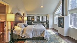 A spacious bedroom with a large bed, a sitting area with a table and chairs, a fireplace, and a view of the outdoors through large windows. - 1 Mi to Mtn, 1 More to Shore! Luxury Tahoe Home (South Lake Tahoe)