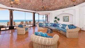 A spacious lounge with a curved sofa set, wicker chairs, and a view of the ocean. - Whale of a Tale – Adults-Only Beachfront (Puerto Peñasco)