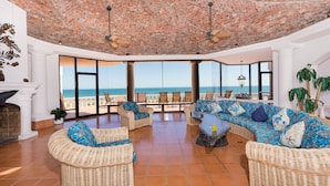A spacious lounge area with wicker furniture, a fireplace, and large windows offering a view of the sea. - Whale of a Tale – Adults-Only Beachfront (Puerto Peñasco)