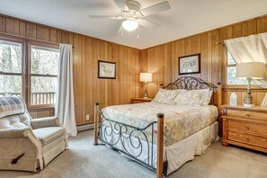 Quarto com cama, cadeira, mesa de cabeceira, luminária e ventilador de teto.