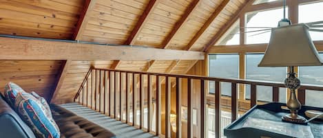 Un intérieur en bois avec un plafond en pente, un banc rembourré avec des coussins, une table avec une lampe et une vue dégagée grâce à de grandes fenêtres.