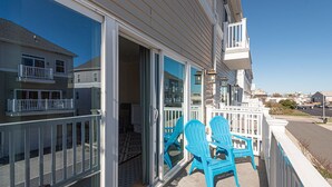 Un balcon avec une balustrade blanche, une porte-fenêtre coulissante et des chaises bleues.