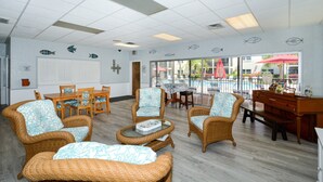 A spacious room with wicker furniture, a dining table, and a view of a pool area. - Condo# 208 Charming Condo at La Siesta with Partial Beach Views "Your home away from home" (Sarasota)
