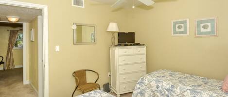A bedroom with two beds, a dresser, a chair, a ceiling fan, and a door leading to another room.