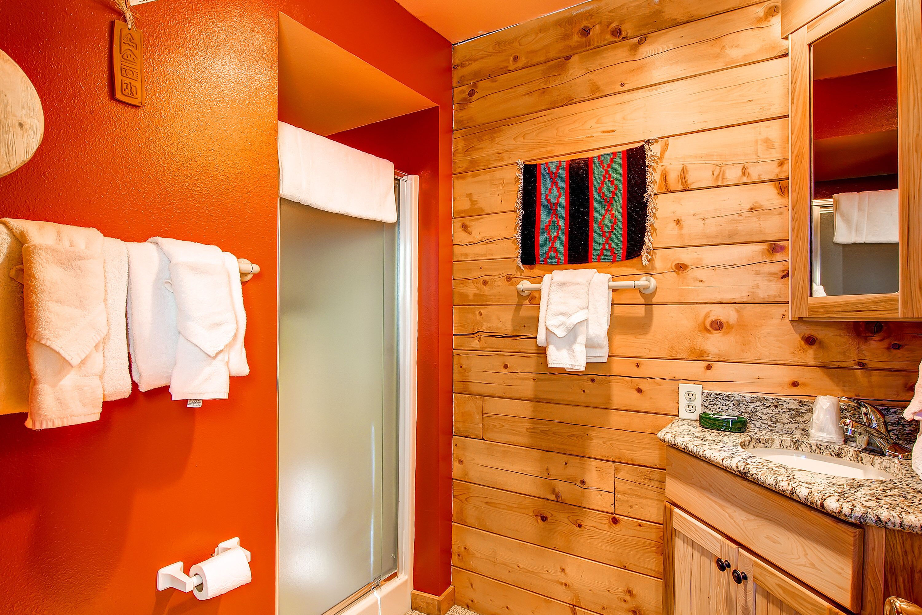 Een badkamer met houten wanden, een glazen douchecabine, een wastafel met een granieten blad en een spiegel boven de wastafel.