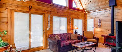 A cozy cabin interior with a wooden interior, a sofa, a chair, a table, and a fireplace.