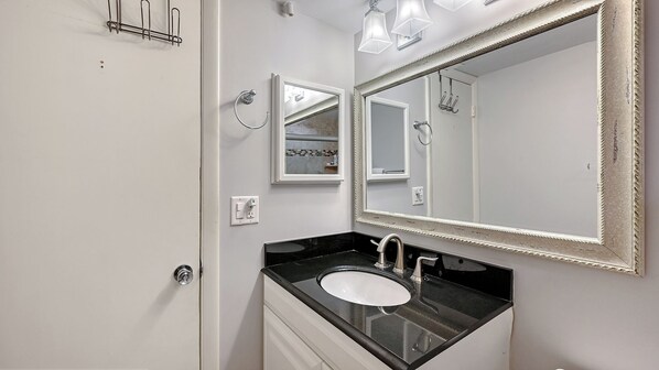 A bathroom with a white vanity, black countertop, and a large mirror with a decorative frame. - Condo# 308 Modern Siesta Key 2BR Condo – Steps from the Beach (Sarasota)