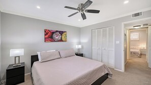 Ein Schlafzimmer mit einem Bett, zwei Nachttischen mit Lampen, einem Deckenventilator, einem Schrank mit Klappläden und einem Bild an der Wand.