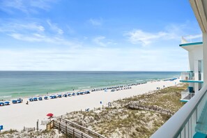 A beach view with a wooden walkway, beach umbrellas, and a building with balconies.
