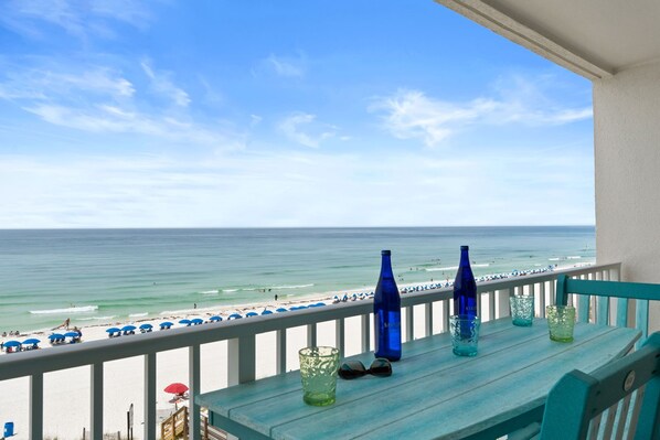 A balcony with a view of the beach, a table with a bottle, and a pair of sunglasses.