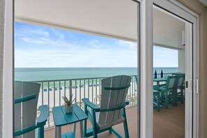 A balcony with a view of the beach, a table with chairs, and a potted plant.