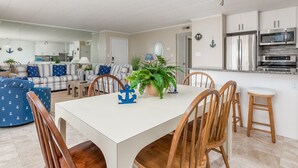 Eine moderne Küche mit Edelstahlgeräten, ein Essbereich mit Holzkohle und ein Wohnzimmer mit Sofa und Topfpflanze.