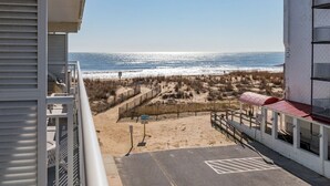 Blick auf den Strand vom Balkon, der Meer, einen Sandstrand und ein Gebäude mit rotem Dach zeigt.