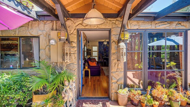 A stone exterior with a wooden ceiling, large windows, and various potted plants. - Bohemian Wonderland: Benicia Bungalow w/ Pergola! (Benicia)