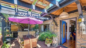 A wooden deck with a table and chairs, surrounded by potted plants and a purple umbrella. - Bohemian Wonderland: Benicia Bungalow w/ Pergola! (Benicia)