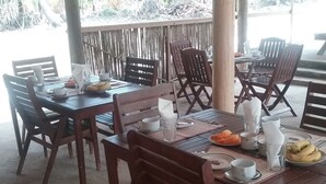 Un espace extérieur abrité, aménagé pour les repas, avec des tables et des chaises en bois.