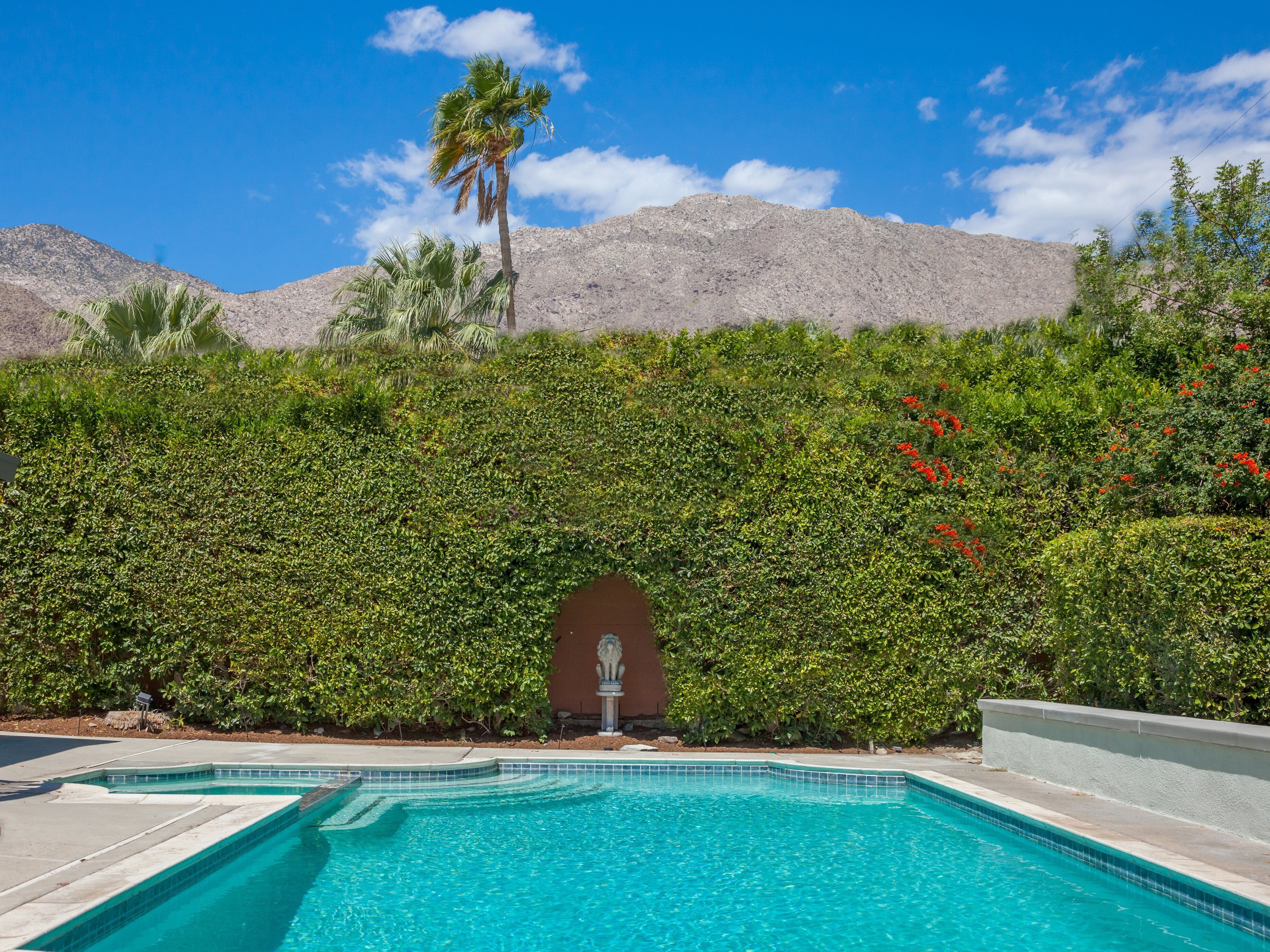 A swimming pool with clear blue water, surrounded by lush greenery and a mountain backdrop.