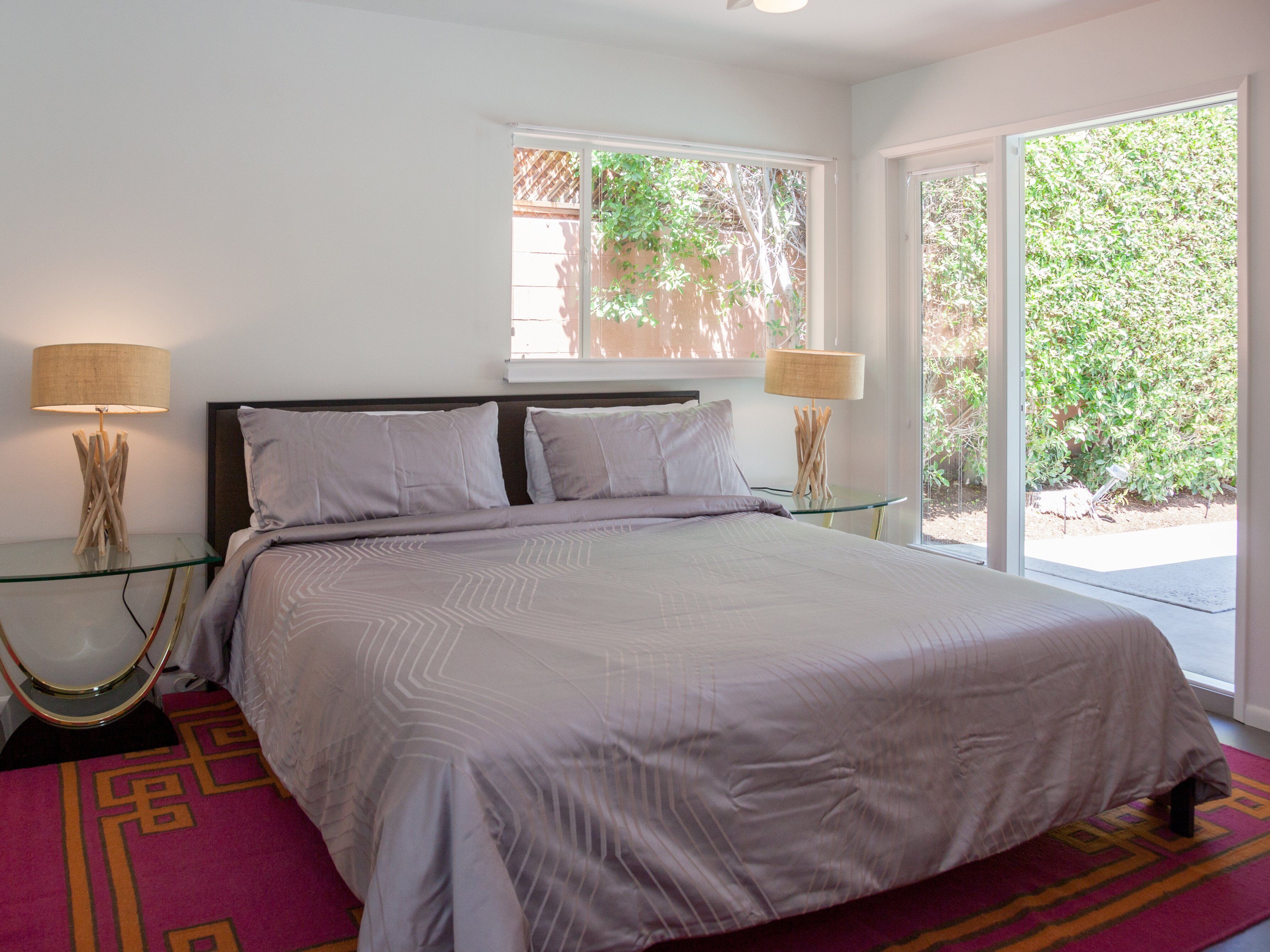 Une chambre à coucher avec un lit, deux tables de chevet, une fen être et une vue sur la verdure.