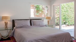 A bedroom with a bed, two bedside tables, a window, and a view of greenery. - The Nest – Mid-Century Palm Springs Retreat (Palm Springs)